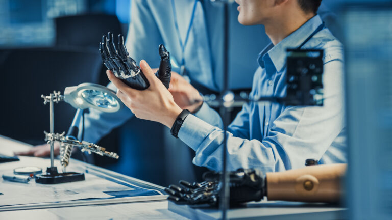 Technological Prosthetic Robot Arm is Tested by Two Professional Development Engineers in a High Tech Research Laboratory with Modern Futuristic Equipment. Compare Data on a Personal Computer